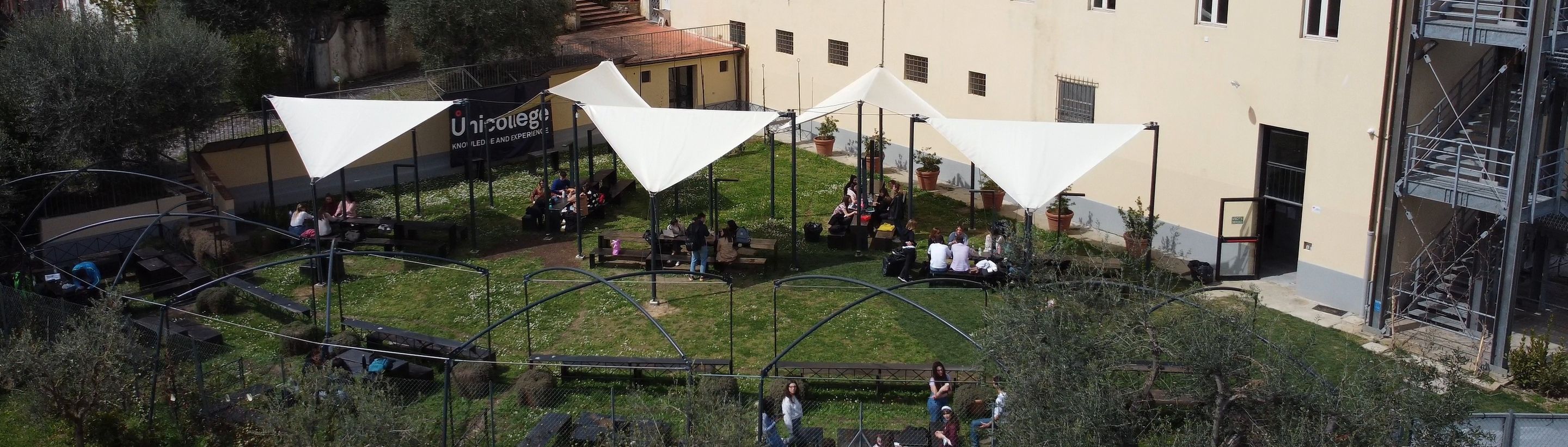 Students sitting under the tents in the garden of the Unicollege Florence campus