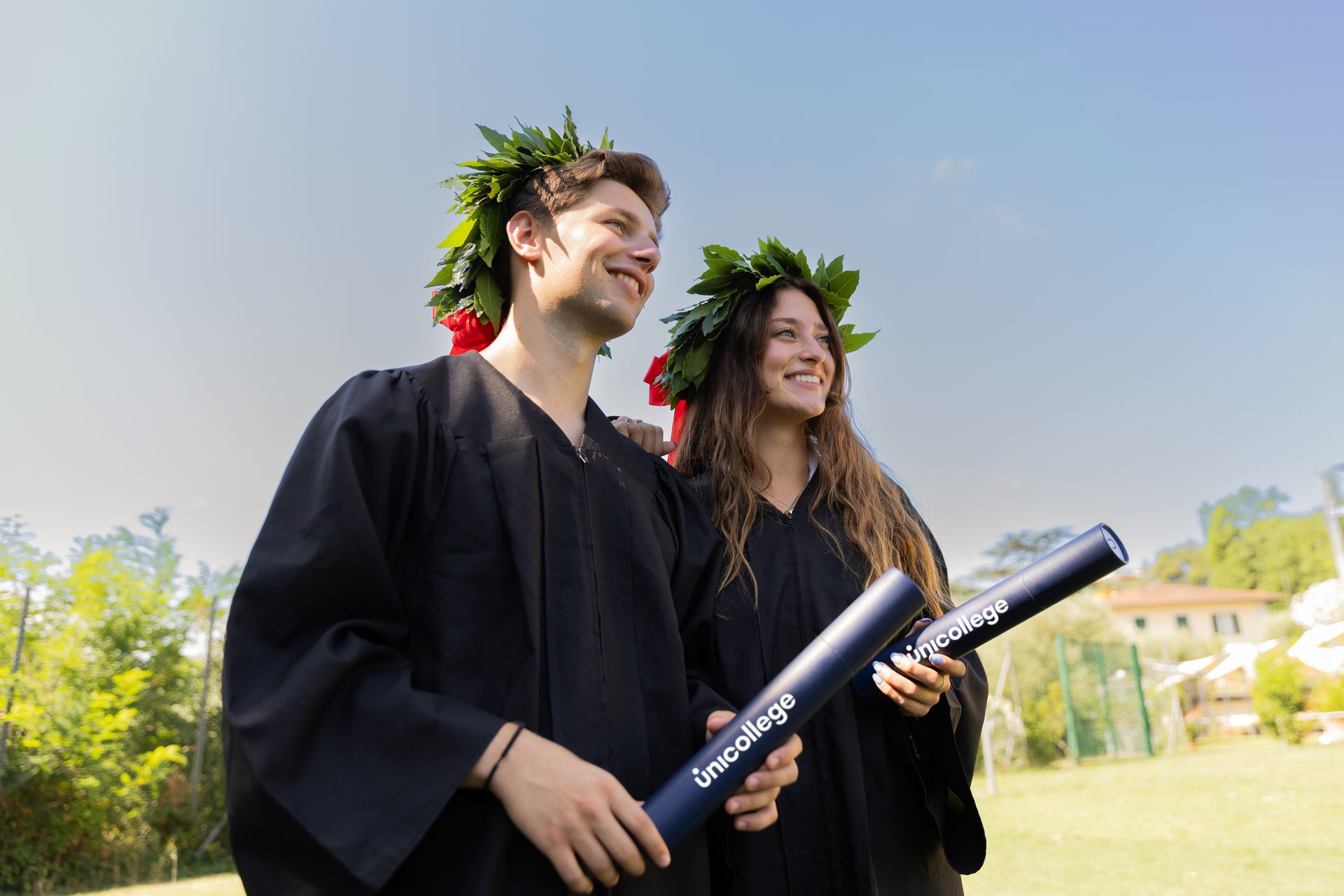 Two Unicollege graduates with laurel wreaths and diploma